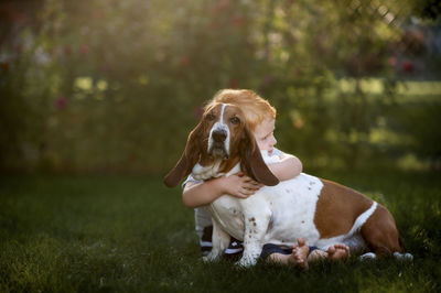 Toddler boy sitting and hugging his hound dog in the backyard grass