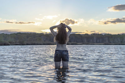 Rear view of shirtless woman standing in lake against sky