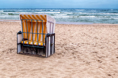 Hooded chair at beach against sky