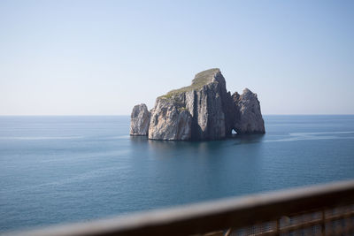 Rock formation in sea against clear sky