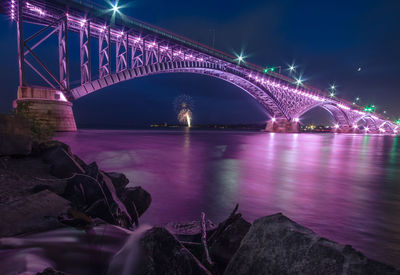 Firework exploding in sky with illuminated bridge over river