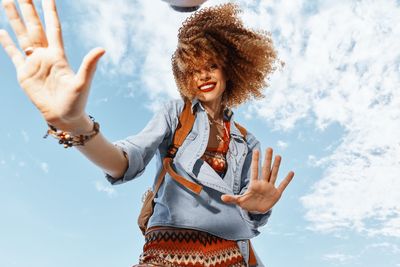 Young woman with arms raised standing against sky