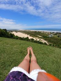 Low section of woman relaxing on land against sky