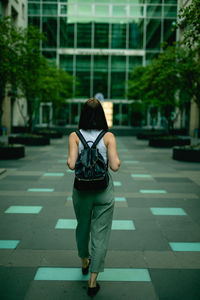 Rear view of young woman walking towards modern building in city