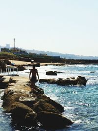 Woman standing on rock by sea against clear sky