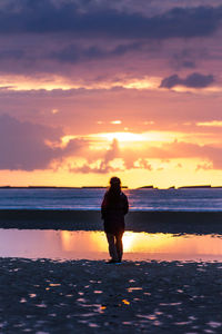 Full length of woman standing on beach against sky during sunset