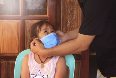 Father getting daughter dressed with face mask at home