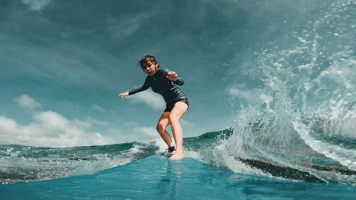 Young woman surfing on sea against sky