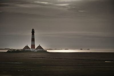 Lighthouse amidst sea and buildings against sky