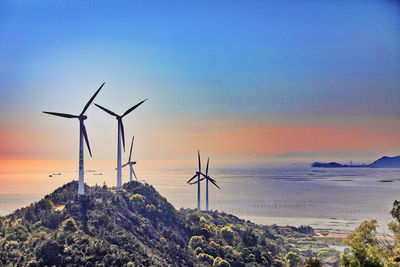 Wind turbines on land against sky during sunset