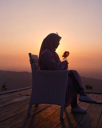 Rear view of woman sitting on chair at sunset