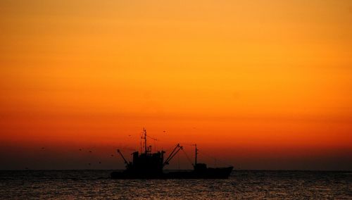 Silhouette ship in sea against orange sky