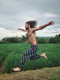 Young man with arms raised on field against sky