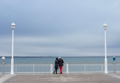 Rear view of couple standing at observation point against cloudy sky