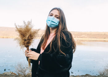 Portrait of young woman using phone while standing against sky