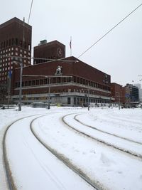 Snow covered road by buildings against sky in city
