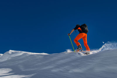 Person skiing on snowcapped mountain against clear blue sky