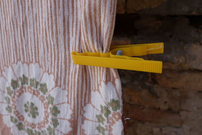 Close-up of yellow clothespin on fabric hanging by brick wall