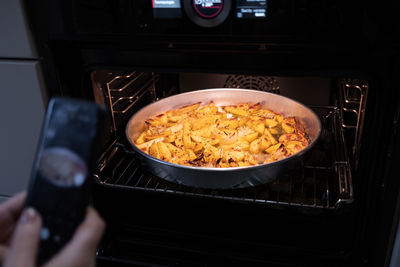 A food blogger takes pictures with phone and shoots food in the oven that she has cooked. 