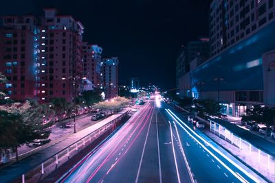 Light trails on city street amidst buildings at night
