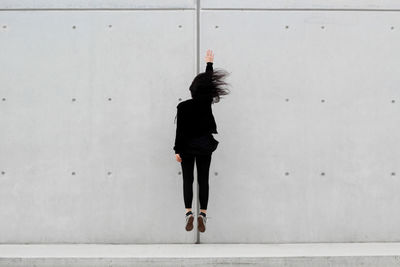 Full length of woman jumping against wall