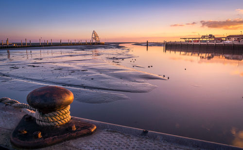 Bollard with rope at harbor against sky during sunset