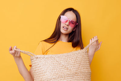 Portrait of young woman wearing sunglasses against yellow background