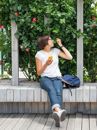 Woman is sniffing trellis roses. pretty woman sits with smartphone in public park. summer vibes.