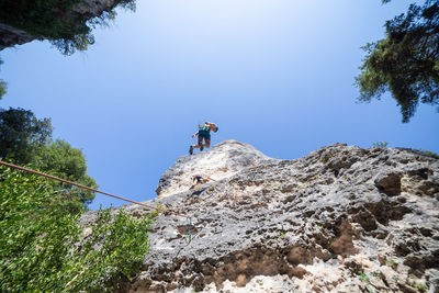 Low angle view of male friends climbing on mountain against clear blue sky