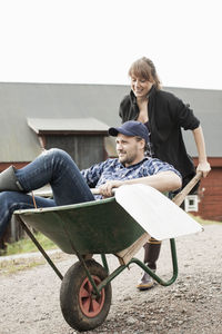 Woman pushing man in wheelbarrow on rural road