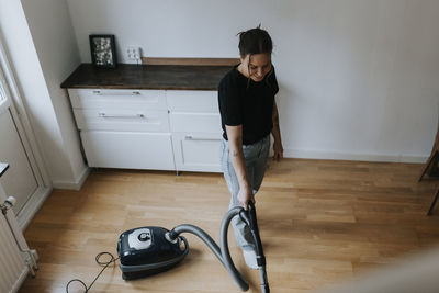 High angle view of young woman vacuum cleaning laminate floor