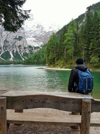 Rear view of man sitting on lake against mountain range