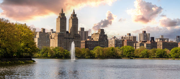 Buildings by river against cloudy sky