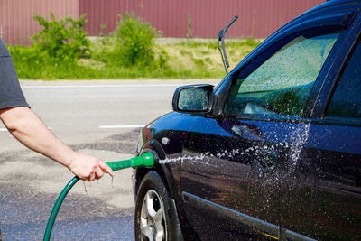 Man is washing car outdoor. male hand holds hose with water and waters vehicle. cleaning car 