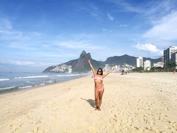 Portrait of happy bikini woman with arms raised standing at beach