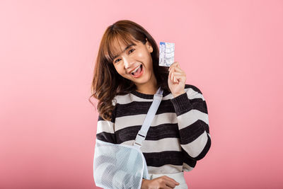 Portrait of young woman standing against pink background