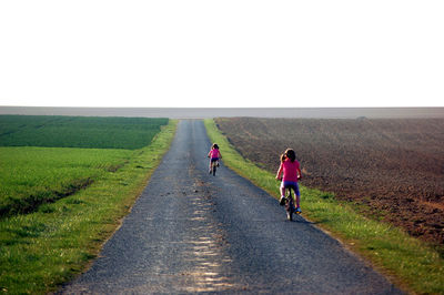 Rear view of girls riding bicycles on road against clear sky