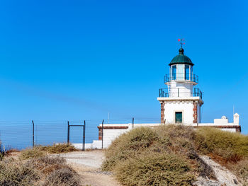 Lighthouse by sea against clear blue sky