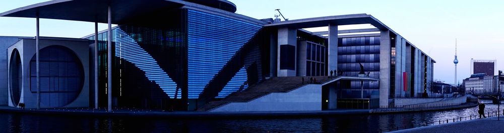 Modern buildings by river against sky in city