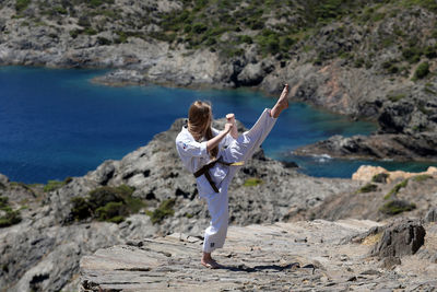 Rear view of woman standing on rock by sea