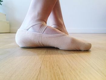 Low section of person wearing ballet shoes on hardwood floor