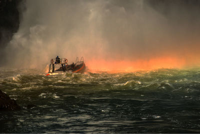 Boat sailing in sea against waterfall during sunset