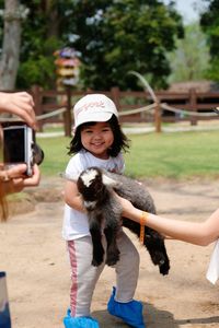 Girl holding kid goat on field
