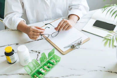 Crop photo of woman nutritionist doctor plus size in white shirt working at table with daily pills 