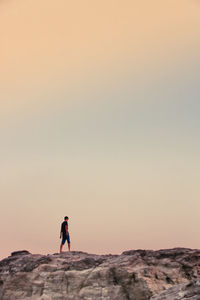 Man standing on rock against sky during sunset