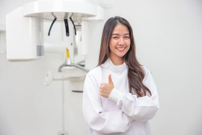 Portrait of smiling young woman holding dentures while standing against wall