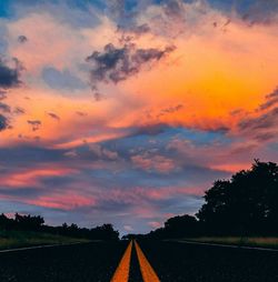 Road by silhouette trees against sky during sunset