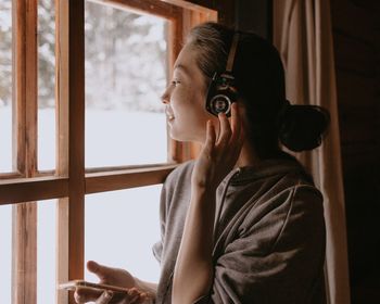 Woman in country house at the window with headphones and mobile phone