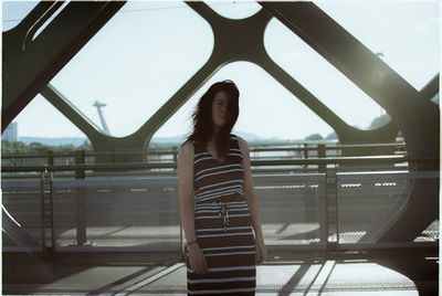 Portrait of young woman standing on railing against sky