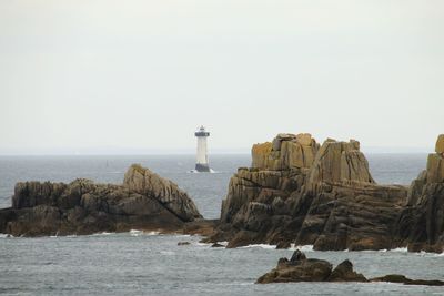 Lighthouse on rock formation by sea against clear sky